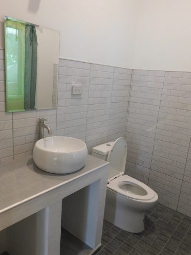 Modern bathroom with a round sink on a countertop and a white toilet in a tiled space.