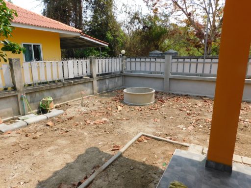 A clearing with bare soil and a circular structure, surrounded by a fence and trees.