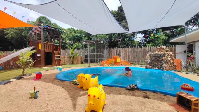 Play area featuring a pool, playground, and colorful decorations under shaded canopies.