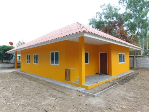 Bright yellow house with a sloped roof and several windows, surrounded by bare ground.