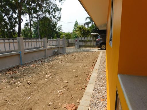 Gravel area beside a bright yellow building with trees in the background.