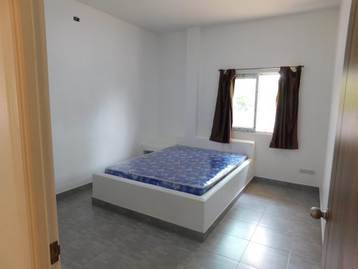 Simple bedroom with a double bed, light walls, and natural light from a window.