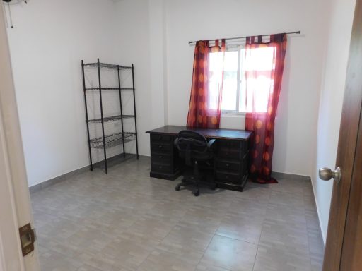 Brightly lit empty room with a desk, chair, and window dressed in red curtains.