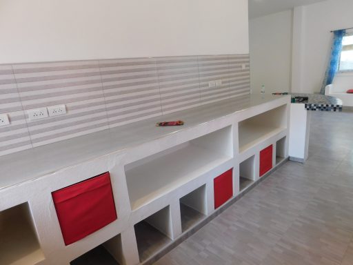 A long white counter with open shelving and red fabric storage bins.