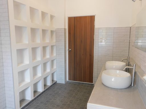 Modern bathroom with two sinks, a wooden door, and wall-mounted shelves.