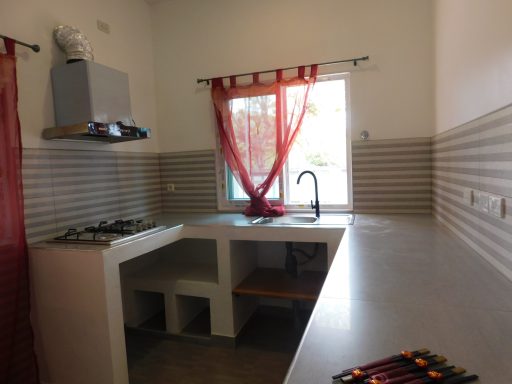 Modern kitchen with a window, red curtains, gas stove, and minimalist countertop.